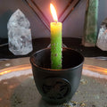 The Money Candle: a green candle dressed with herbs, lit in a black holder on an altar plate, with crystal points behind it