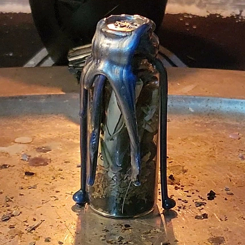 A small glass spell jar sealed with black and silver wax, close up, with herbs showing through the glass