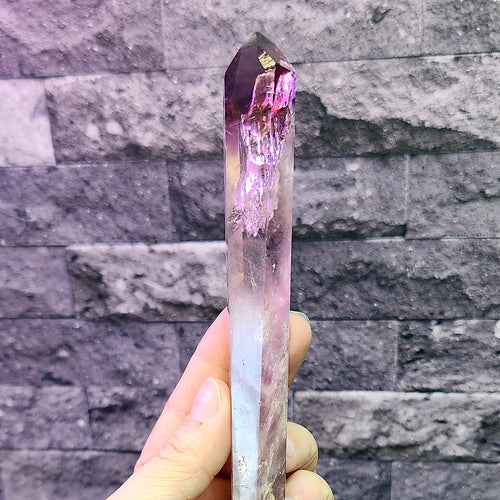 How to Cleanse a Stone and Set an Intention in It: a hand holding a long amethyst point, purple at the tip and clear toward the base